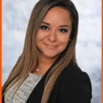 Angelica Brager, team member at Loqal Marketing, is pictured with long straight hair, wearing a black blazer over a light top, smiling confidently in a professional studio portrait against a light gray background.